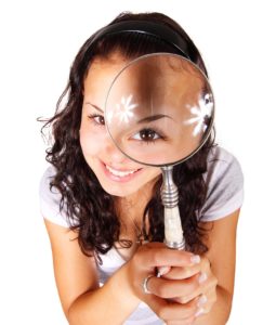 woman with long brown hair looking through a magnifying glass and smiling